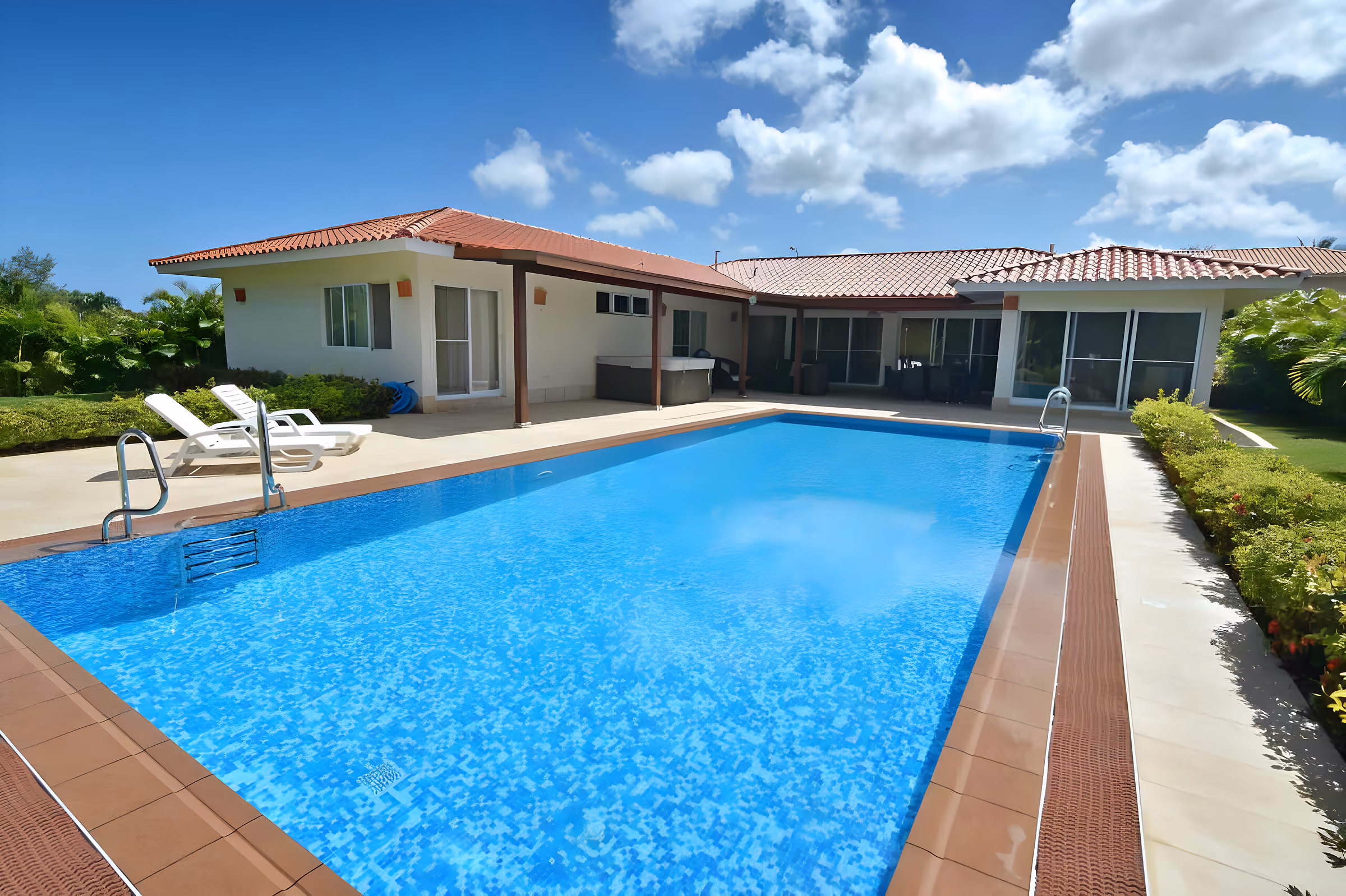 Готовият басейн зад къщата с керемиден покрив, заобиколен от тропическа растителност